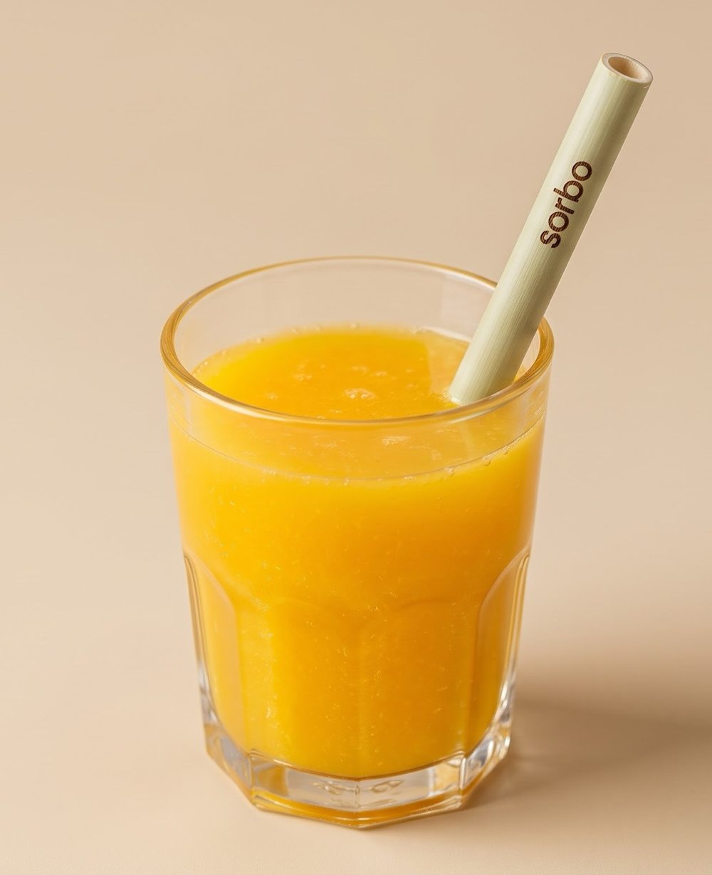 Pitillo Sorbo de carrizo verde claro con la palabra sorbo grabada, dentro de un vaso de jugo de naranja